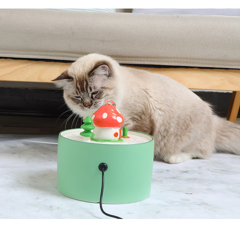 Cat drinking from a green automatic pet water dispenser shaped like a mushroom house on the floor