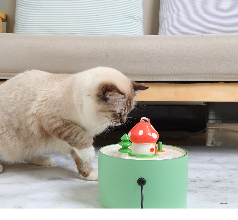 Cat drinking from a green automatic pet water dispenser with a red mushroom decoration