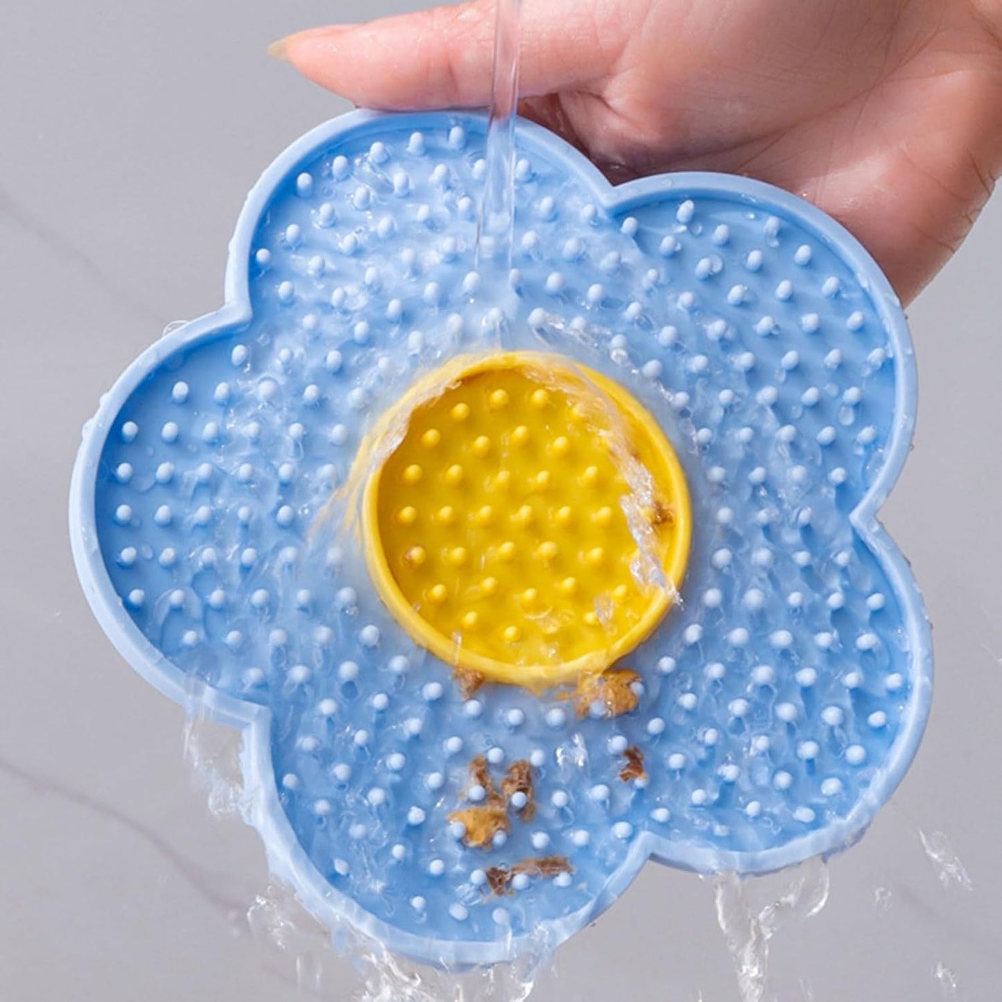 Blue and yellow Cats Lick Pad With Suctions shaped like a flower with water pouring over it for easy cleaning