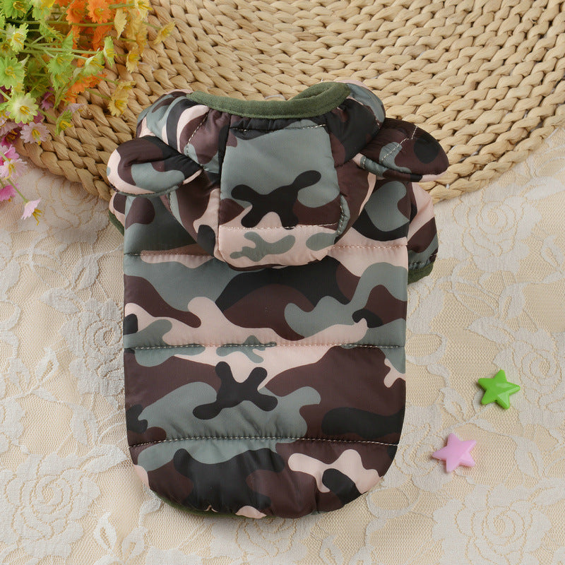 Camouflage-patterned pet coat on a textured surface with flowers and a woven mat in the background