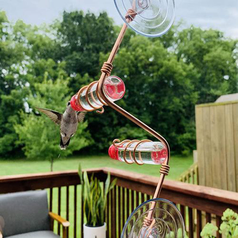 Copper spiral Garden Bird Feeder with red nectar tubes attracting a hummingbird on a wooden deck