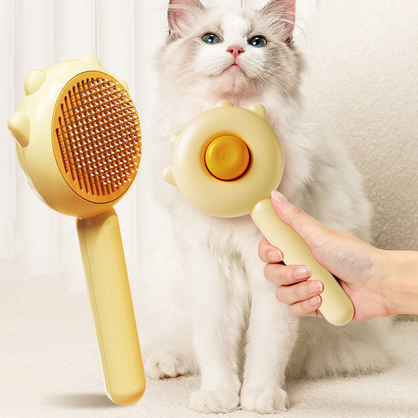 Person holding a yellow pet grooming brush next to a white cat