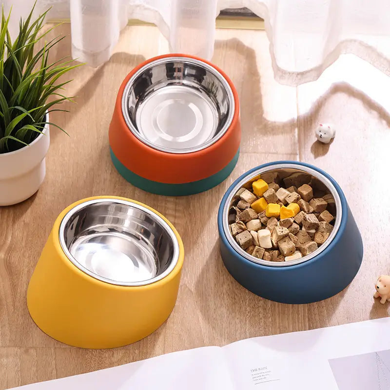 Three colorful pet bowls on a wooden surface with one containing pet food.